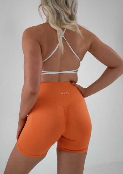 Model wearing orange activewear shorts and white bra set