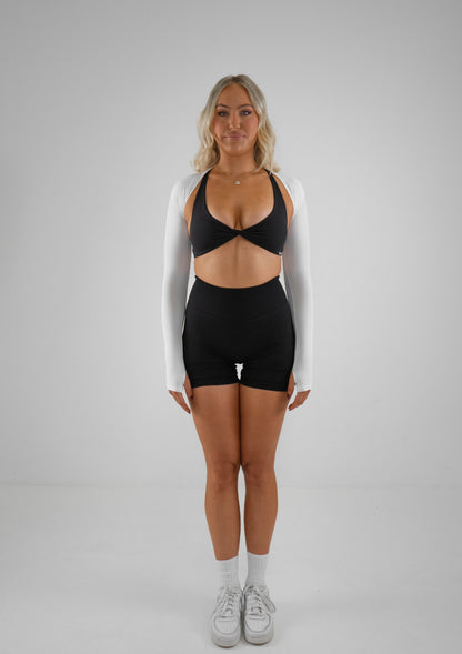 Model wearing black activewear shorts and bra set with white bolero